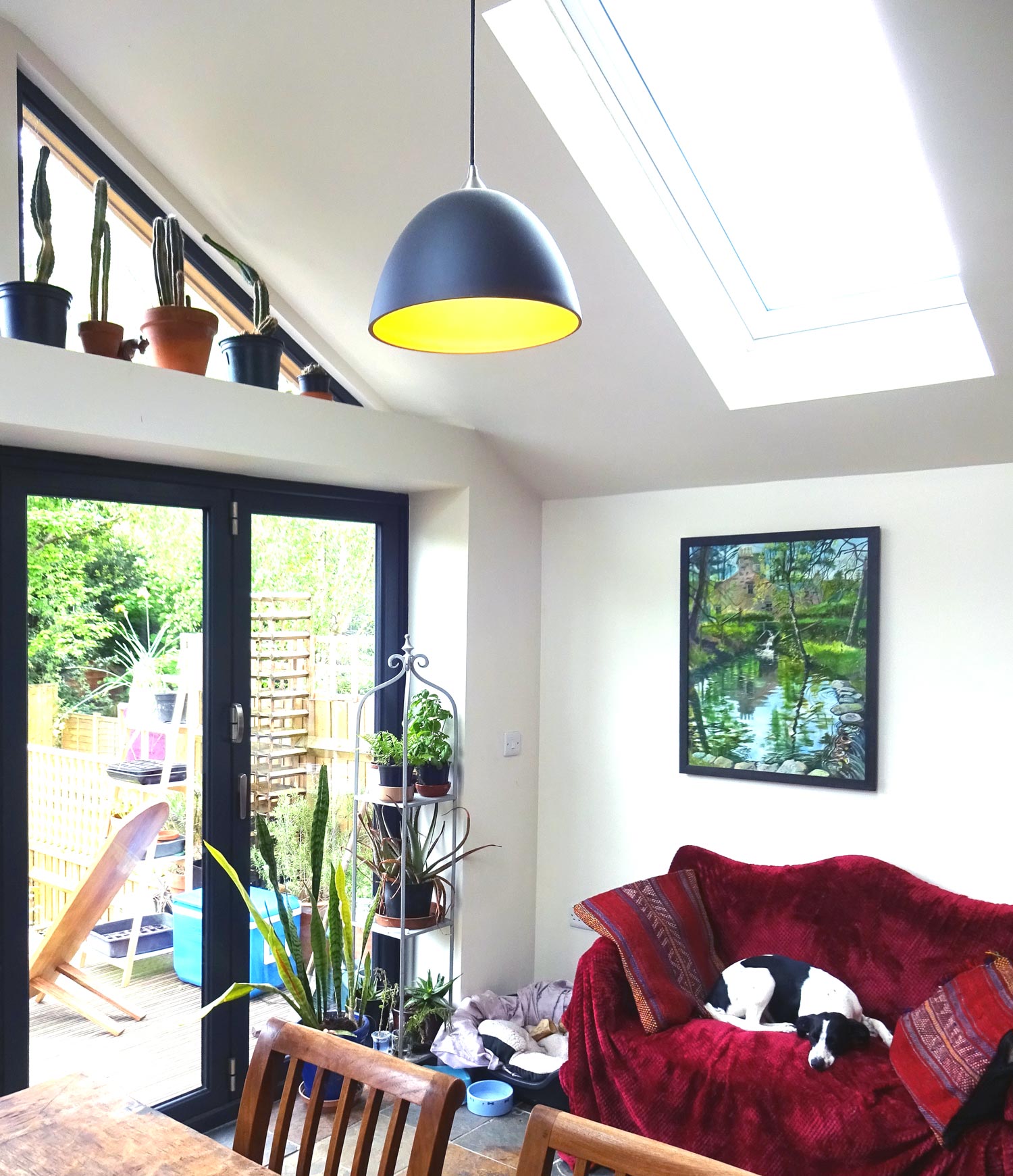 interior view of glazed gable with pendant light over dining table and dog asleep on red sofa 